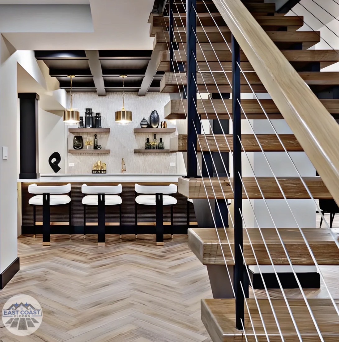 Herringbone flooring with floating staircase and bar by East Coast Floors